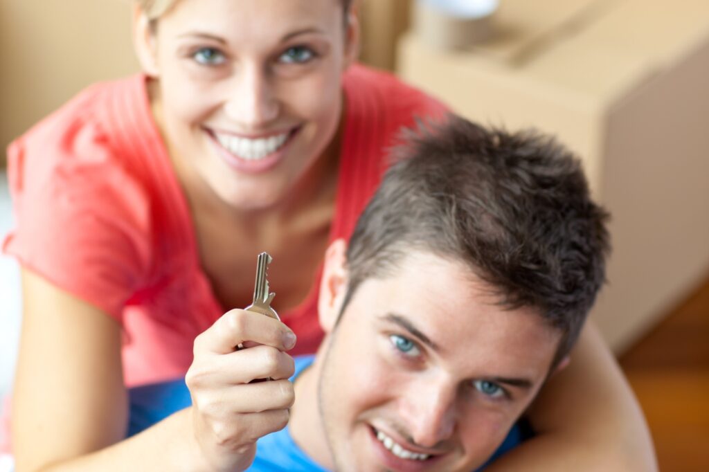 A young couple is holding a key to their new flat and is surrounded by carton; in the concept of moving to Clapham.