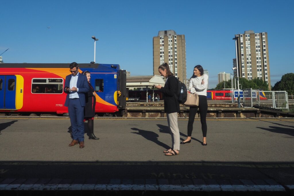 Passengers in Clapham Junction Station's platform in the concept of 'how to use Clapham's public transport'.